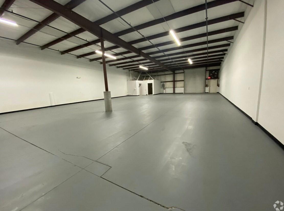 An empty industrial warehouse space features gray concrete floors, white walls, and exposed ceiling beams — 6555 Garden Road, Riviera Beach FL 33404, RIVIERA BEACH, FL