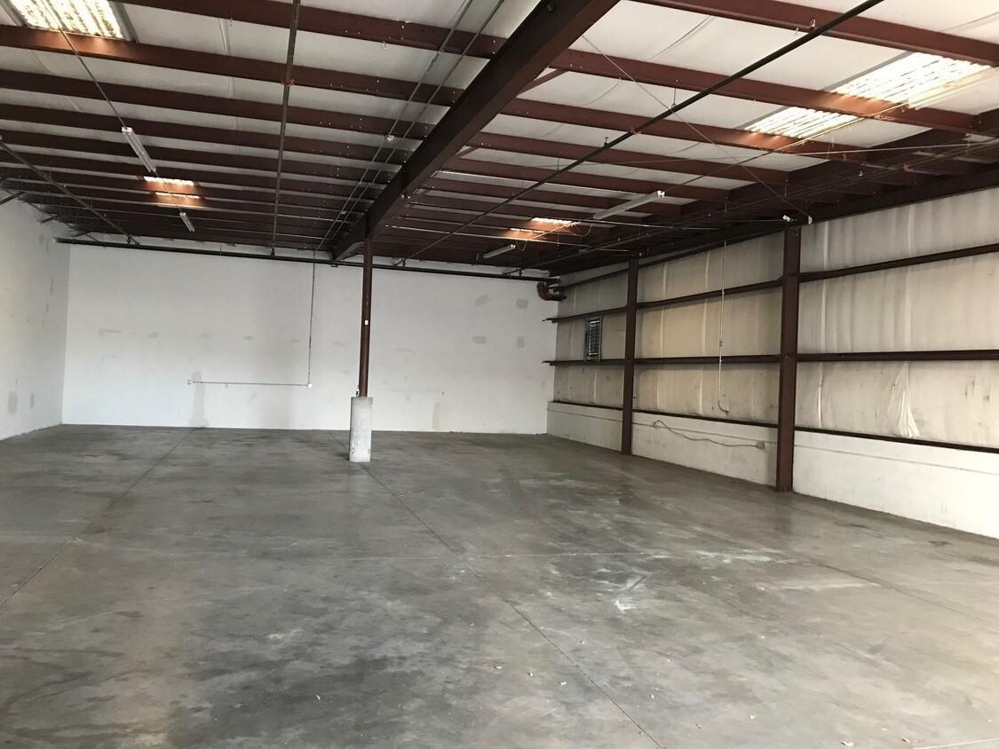An empty warehouse space features a concrete floor, exposed steel beams, and white walls — 6555 Garden Road, Riviera Beach FL 33404, RIVIERA BEACH, FL