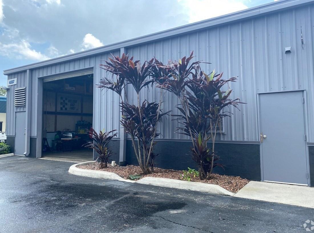 The exterior of a gray metal industrial building features a garage bay and landscaping — 6555 Garden Road, Riviera Beach FL 33404, RIVIERA BEACH, FL
