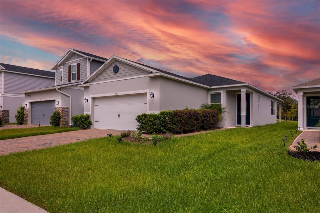 A single-story suburban house with a two-car garage and a green lawn at sunset — 2927 SANCTUARY DRIVE, CLERMONT, FL
