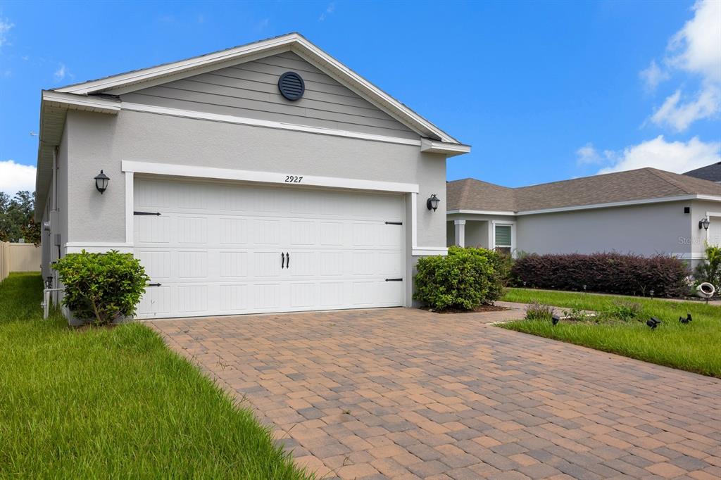 A single-story house with a white garage door, gray siding, and a paver driveway — 2927 SANCTUARY DRIVE, CLERMONT, FL