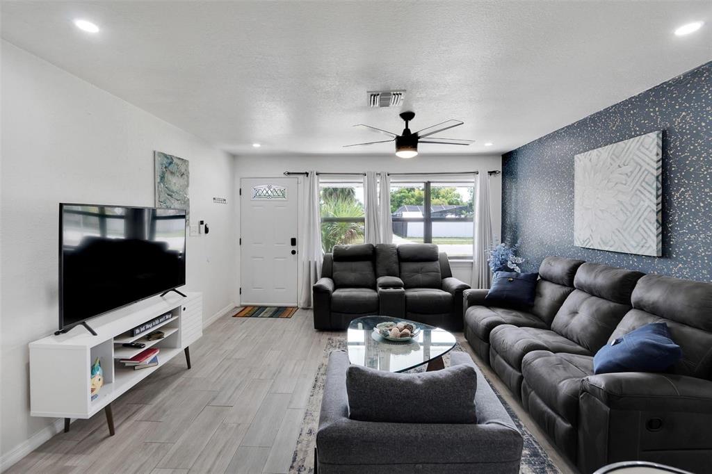 A living room features gray wood-look flooring, a dark accent wall, and gray furniture — 4731 W MONTGOMERY AVENUE, TAMPA, FL
