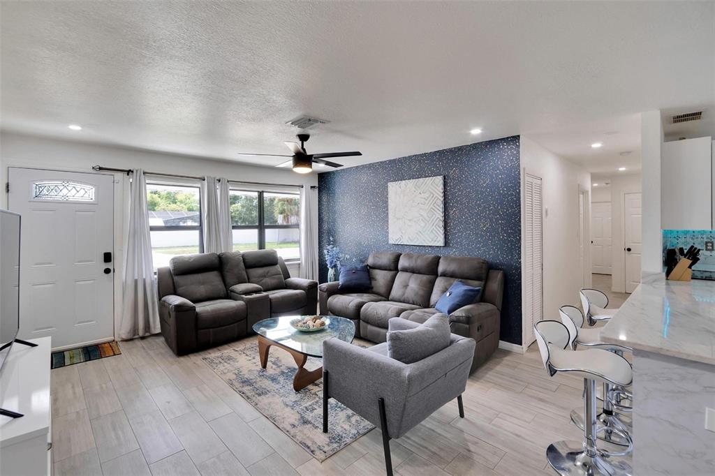 A living room features a dark blue accent wall, gray furniture, and light wood-look flooring — 4731 W MONTGOMERY AVENUE, TAMPA, FL