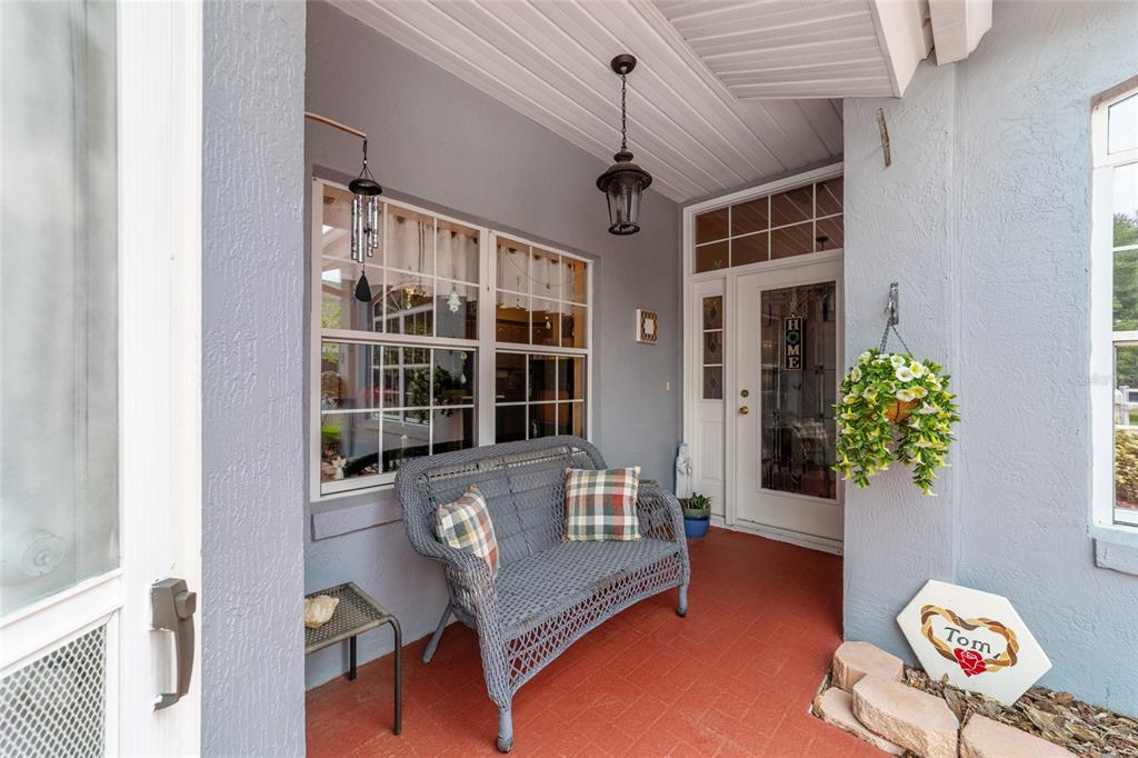 A covered front porch features a gray wicker bench, red brick flooring, and a door — 11460 SW 78TH CIRCLE, OCALA, FL