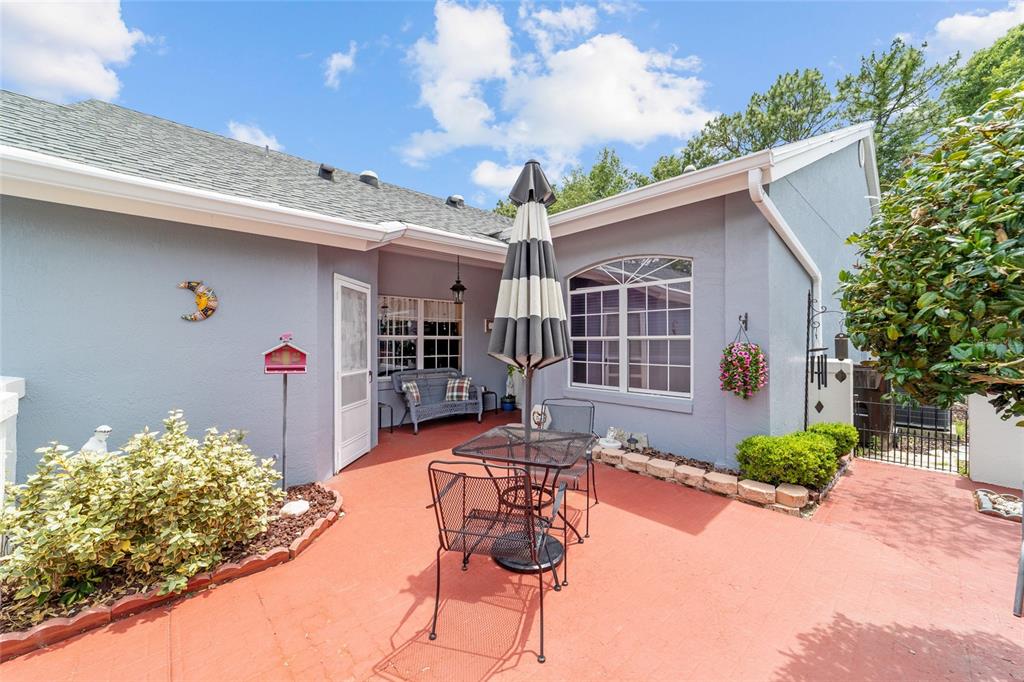 A patio with a table, umbrella, and chairs sits outside a gray house with windows — 11460 SW 78TH CIRCLE, OCALA, FL