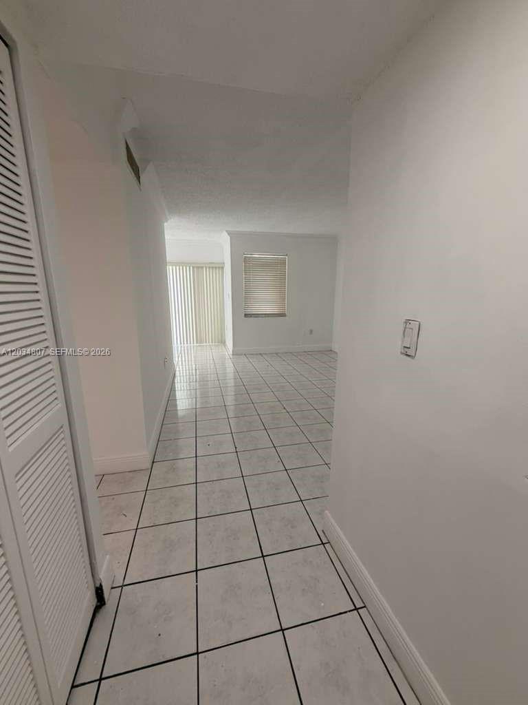 A hallway with white tile flooring leads into an open living area with sliding doors — 9311 SW 4th St # 117B, Miami FL 33174, MIAMI, FL