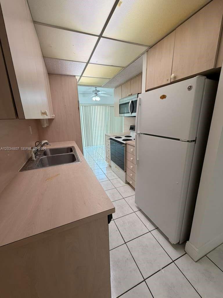 A galley kitchen features light wood cabinets, white appliances, and white tile flooring — 9311 SW 4th St # 117B, Miami FL 33174, MIAMI, FL
