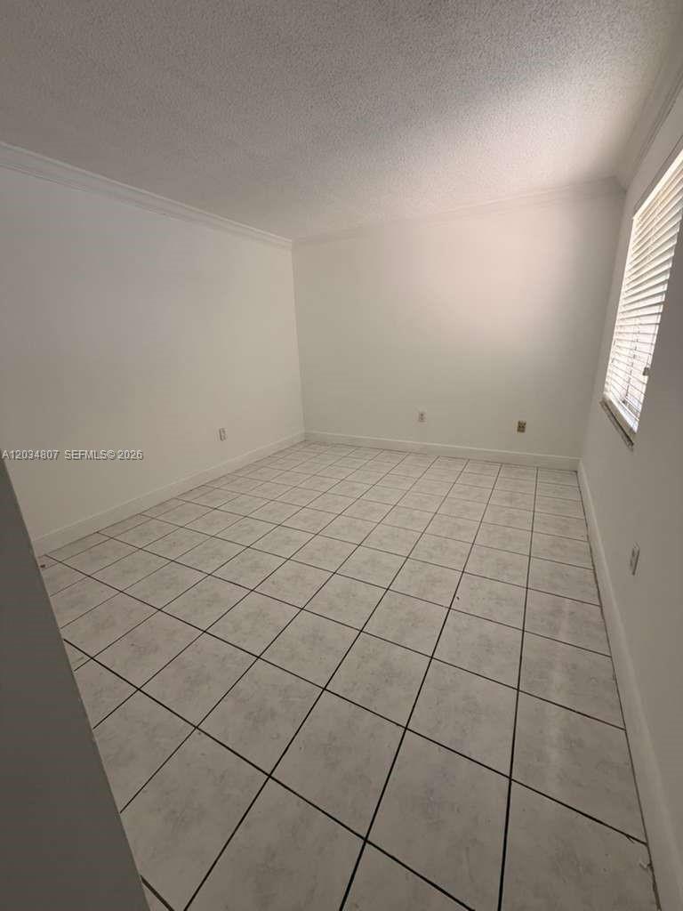 An empty room features white walls, crown molding, and light-colored square floor tiles — 9311 SW 4th St # 117B, Miami FL 33174, MIAMI, FL