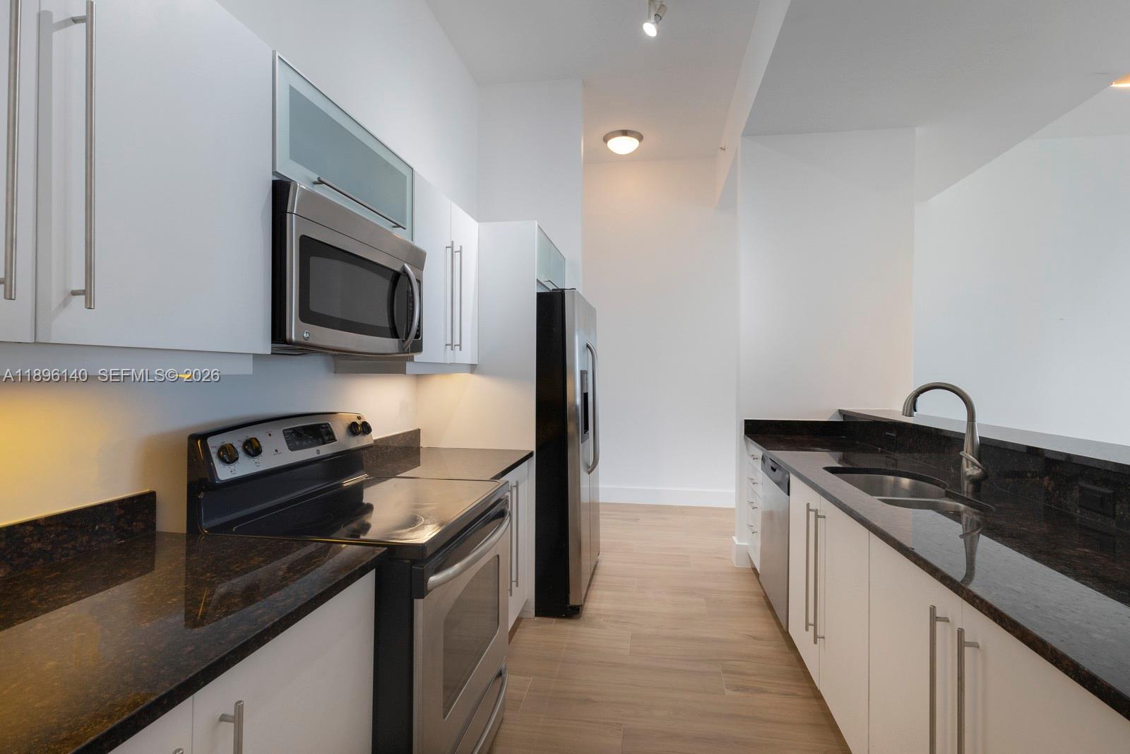 A modern kitchen features white cabinets, dark granite countertops, and stainless steel appliances — 7350 SW 89th St # 514S, Miami FL 33156, MIAMI, FL