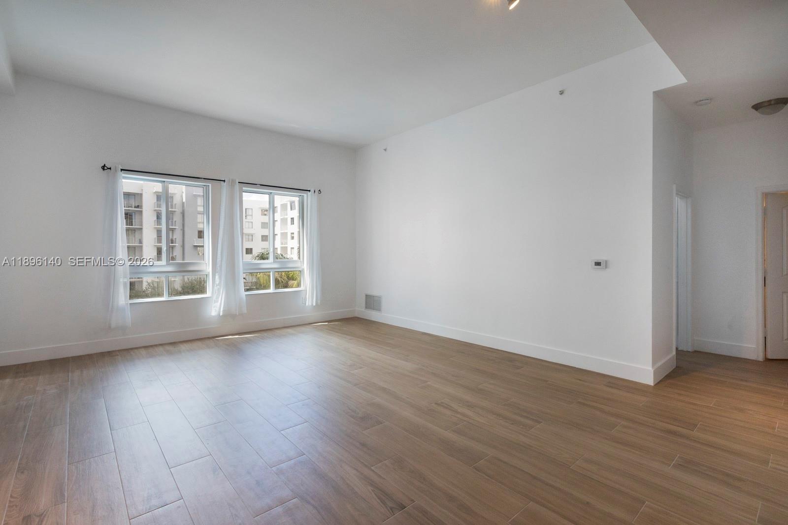 An empty room features white walls, light wood-look tile flooring, and two windows with curtains — 7350 SW 89th St # 514S, Miami FL 33156, MIAMI, FL