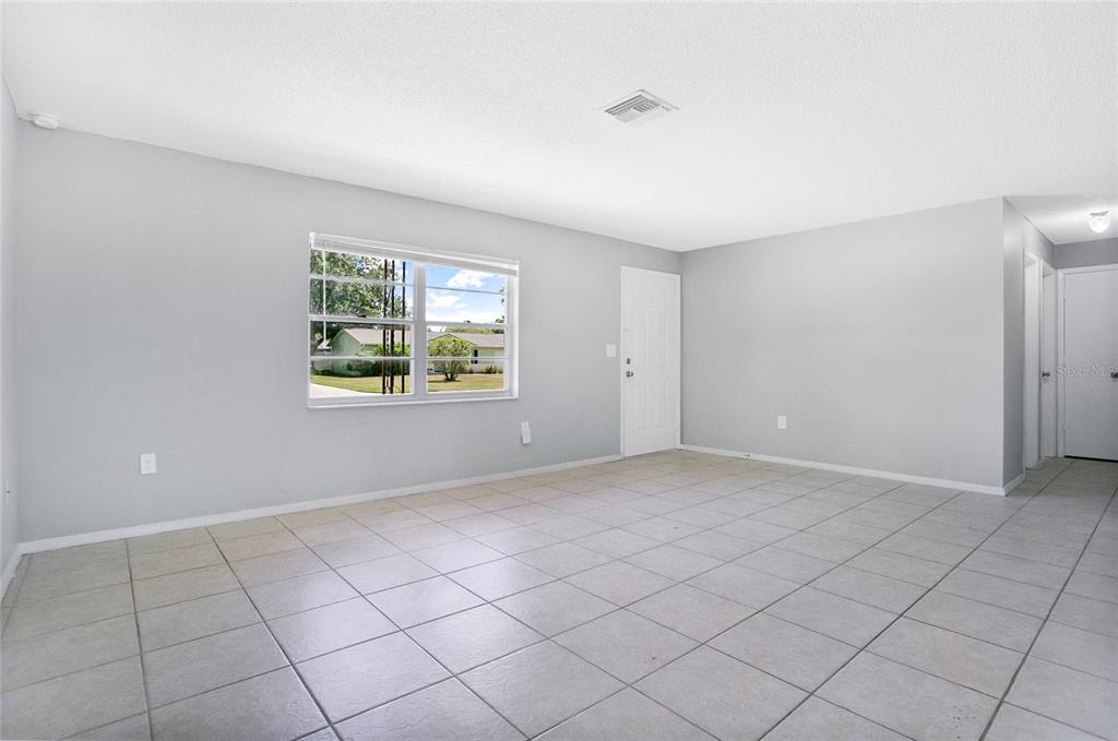 A bright, empty living room features light gray walls, large white floor tiles, and a window — 405 LONG DRIVE, POINCIANA, FL