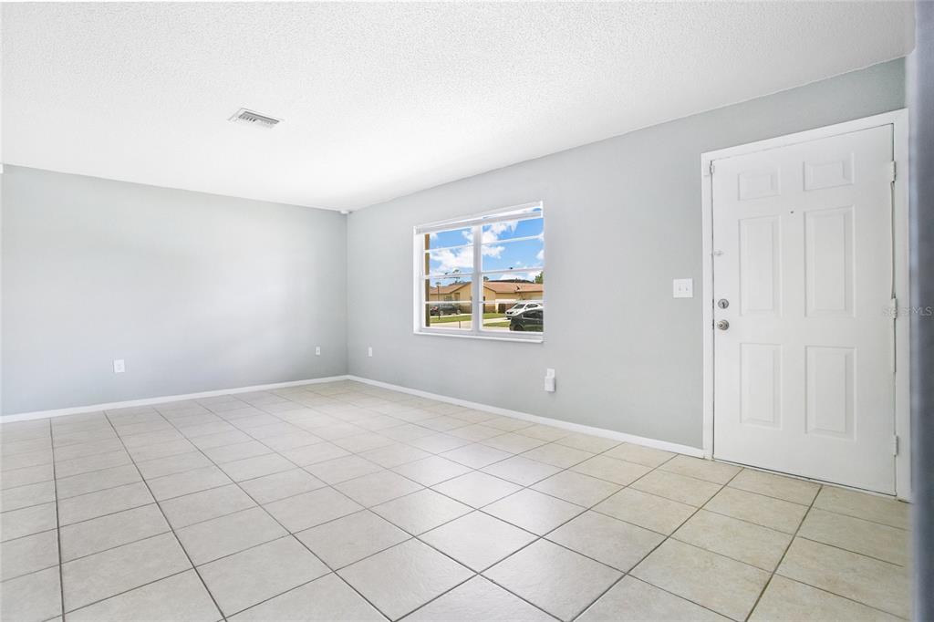 An empty room with light gray walls, white tile flooring, and a single front door — 405 LONG DRIVE, POINCIANA, FL