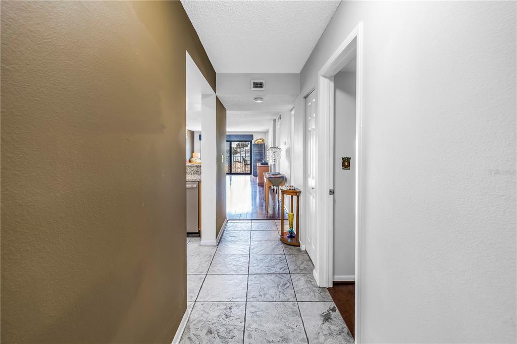A tiled hallway leads past a kitchen and closet toward a sunlit living area — 650 ISLAND WAY UNIT 204, CLEARWATER BEACH, FL