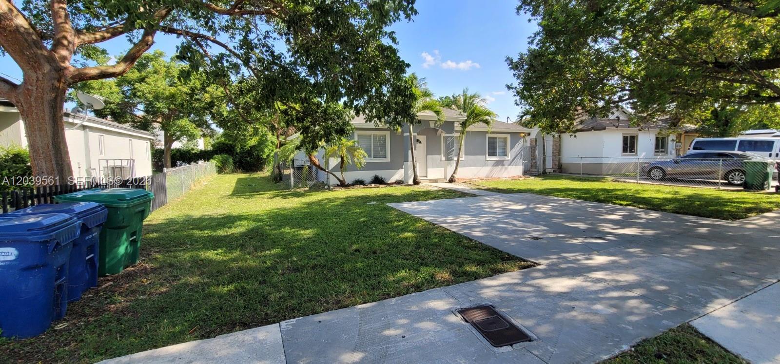 A single-story gray house with a concrete driveway and a front lawn under large trees — 10250 SW 173rd Ter, Miami FL 33157, MIAMI, FL