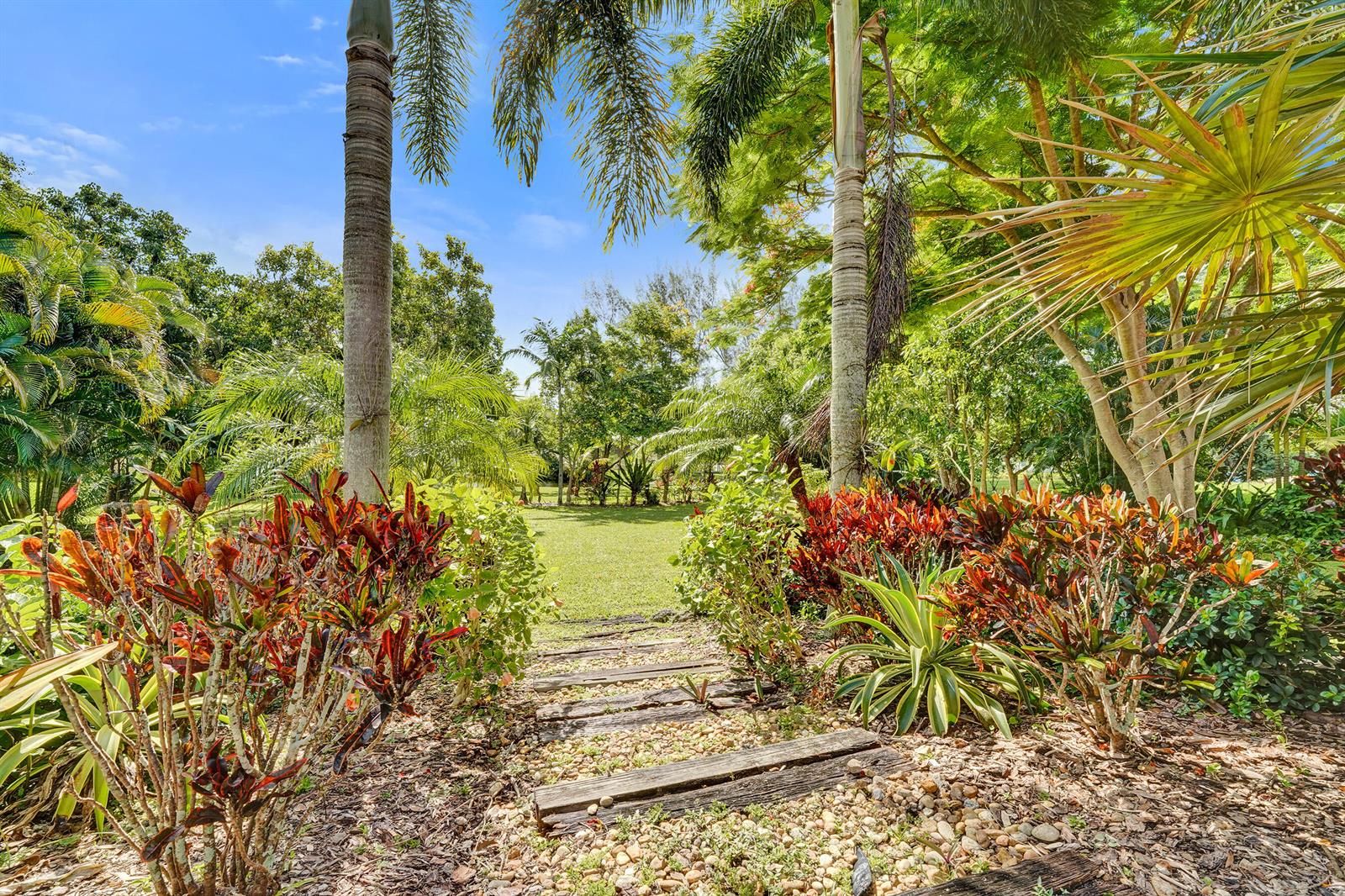 A stone path with wooden steps leads through a tropical garden toward a grassy lawn — 3951 SW 137th Avenue, Miramar FL 33027, MIRAMAR, FL