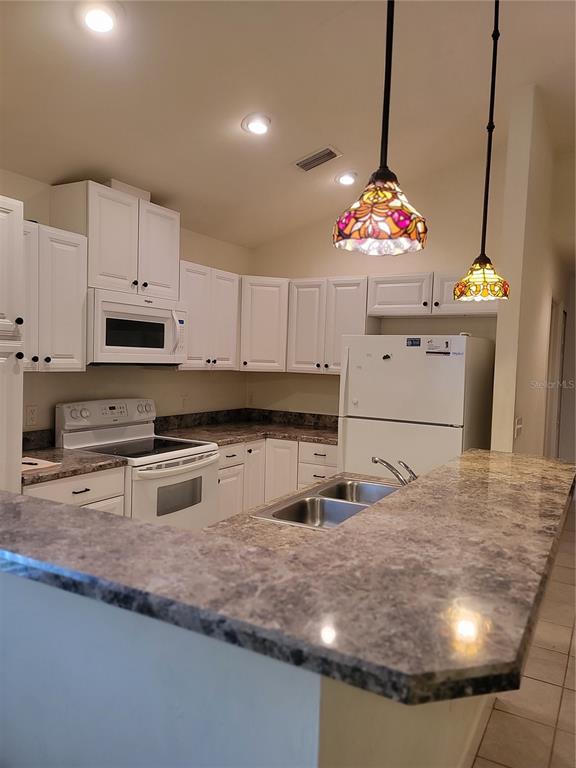 A kitchen features white cabinets, a white stove, a white refrigerator, and a stone-look countertop — 6312 NW 109TH PLACE, ALACHUA, FL