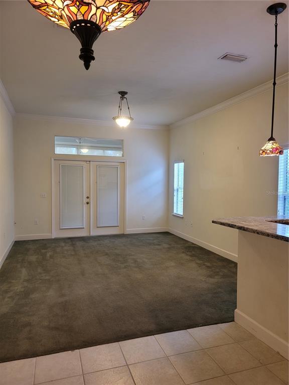 A room with dark carpeting, a tiled kitchen area, and three hanging stained-glass light fixtures — 6312 NW 109TH PLACE, ALACHUA, FL