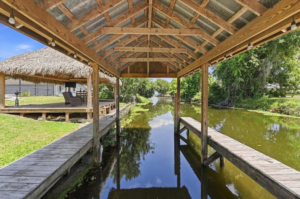 A wooden boat dock with a covered slip sits beside a canal and tiki hut — 2770 LAKE PIERCE DRIVE, LAKE WALES, FL