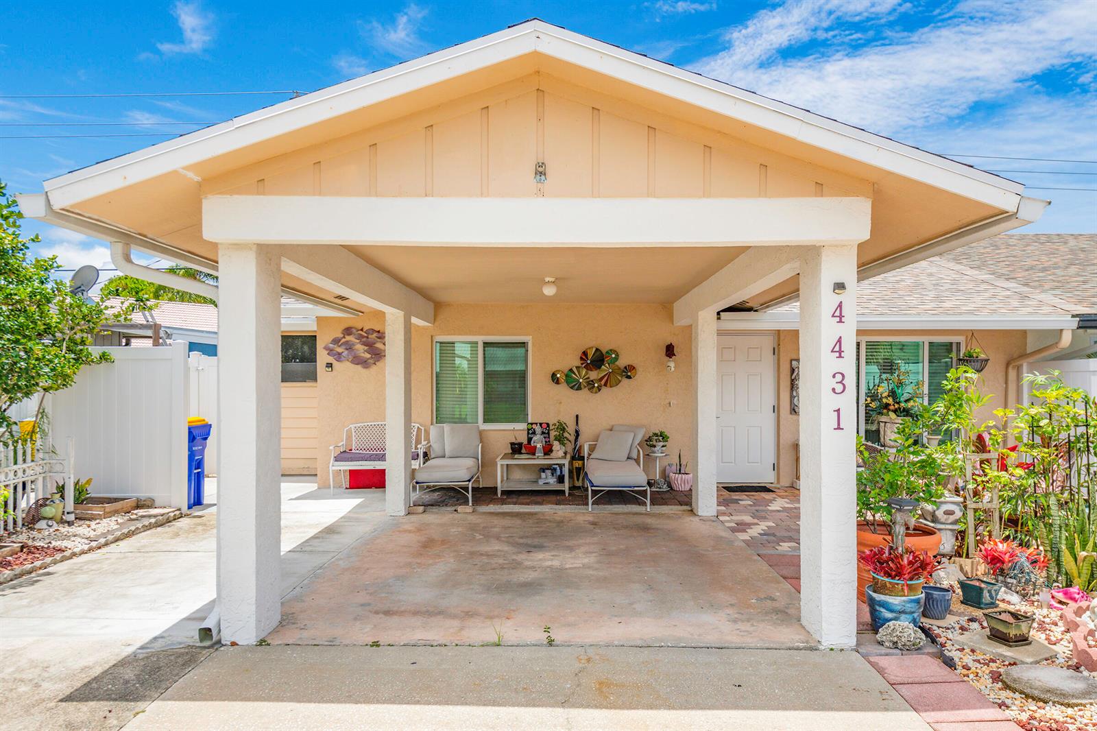 A beige house features a covered carport with a concrete floor and outdoor seating area — 4431 SE Village Road, Stuart FL 34997, STUART, FL