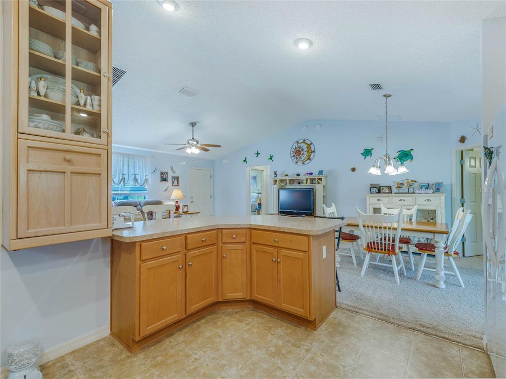 A kitchen with light wood cabinets and a breakfast bar overlooks a carpeted dining area — 1704 LISETTE WAY, THE VILLAGES, FL
