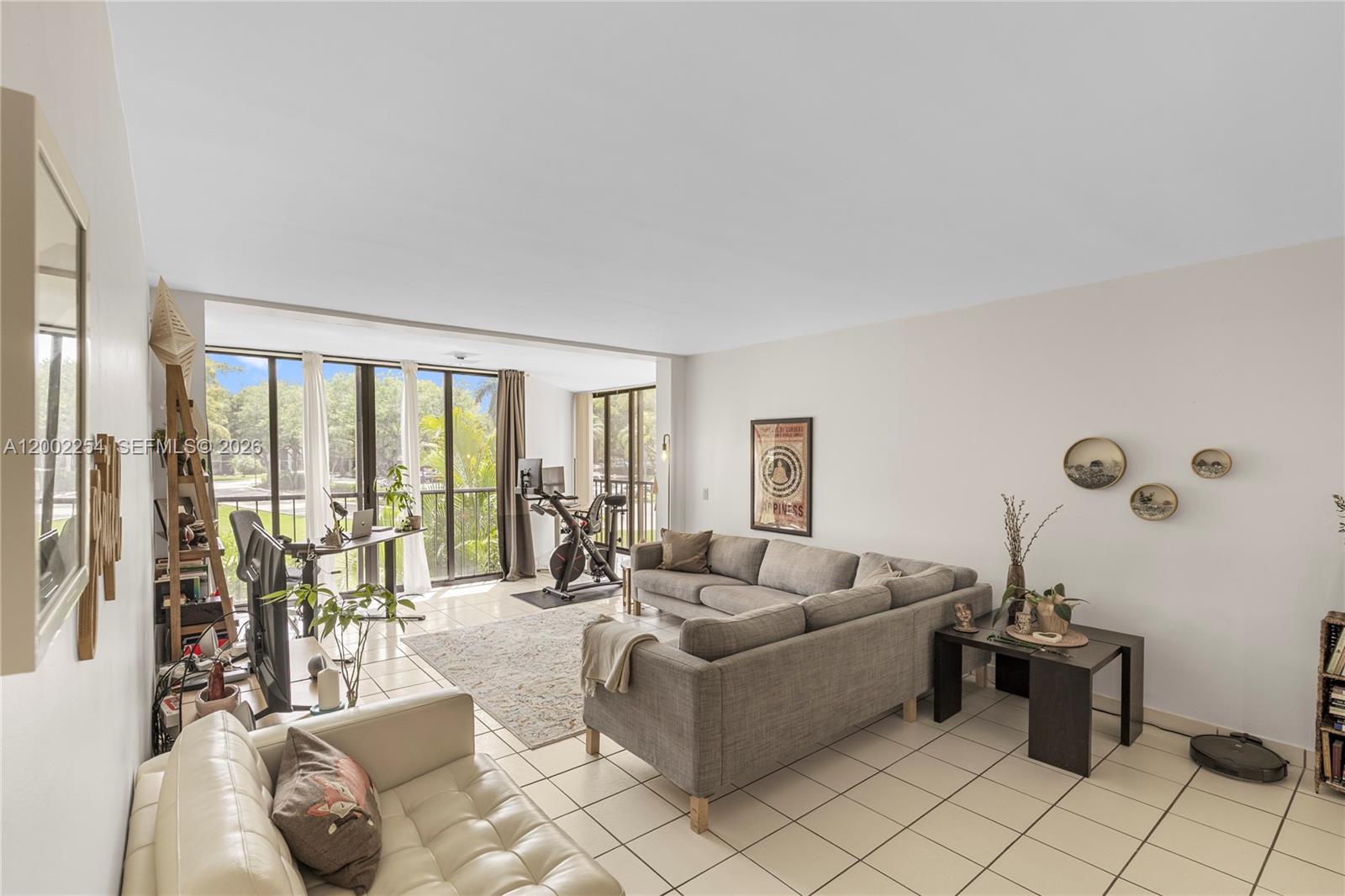 A living room features a sectional sofa, a desk, an exercise bike, and tile flooring — 16175 Golf Club Rd # 212, Weston FL 33326, WESTON, FL