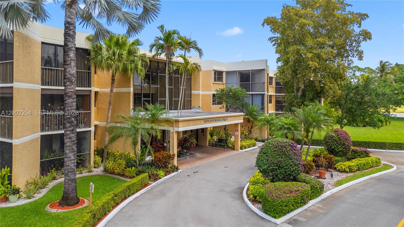 An exterior view of a multi-story apartment building with a circular driveway and landscaping — 16175 Golf Club Rd # 212, Weston FL 33326, WESTON, FL