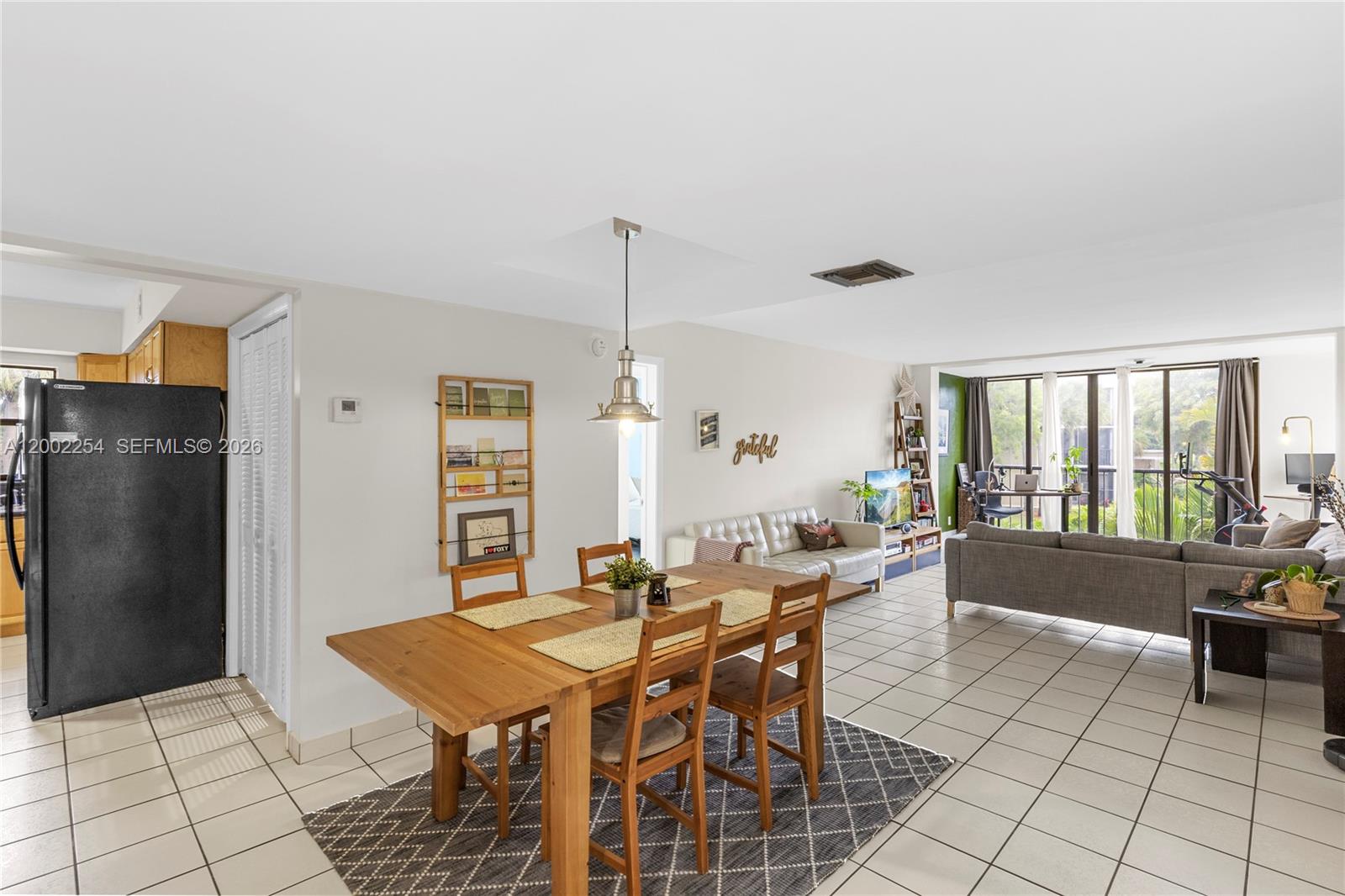 An open-concept living and dining area features tile flooring, a wooden table, and a balcony — 16175 Golf Club Rd # 212, Weston FL 33326, WESTON, FL