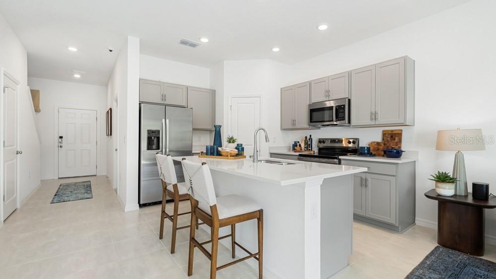 A modern kitchen features gray cabinets, stainless steel appliances, a white island, and bar stools — 7109 PINELIT COVE, NOKOMIS, FL