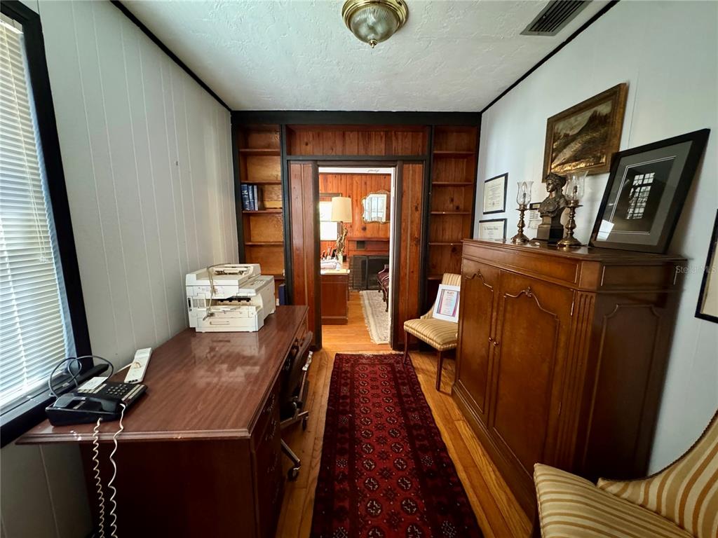 A home office features wood-paneled walls, built-in shelving, a desk, and a patterned area rug — 1215 NW 12TH AVENUE, GAINESVILLE, FL