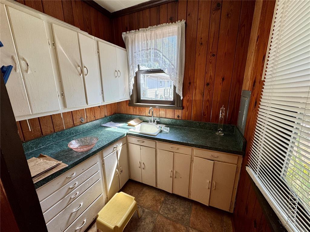 A small kitchen features wood-paneled walls, white cabinets, green laminate countertops, and a single sink — 1215 NW 12TH AVENUE, GAINESVILLE, FL