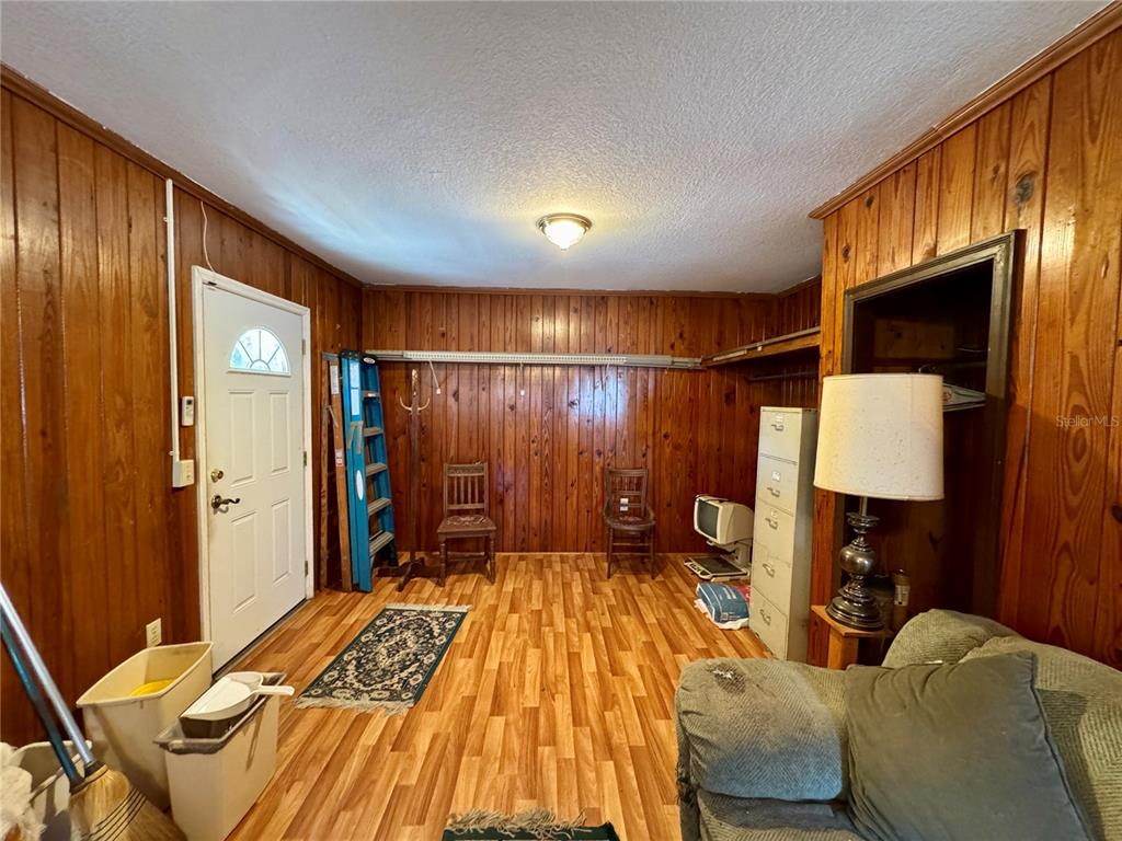 A room with wood-paneled walls, wood-look flooring, a white door, and a ceiling light fixture — 1215 NW 12TH AVENUE, GAINESVILLE, FL