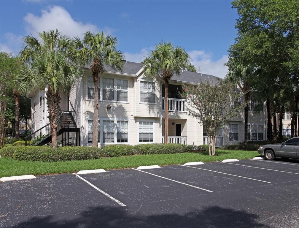 A two-story apartment building with beige siding, balconies, and palm trees sits by a parking lot — 1017 S HIAWASSEE ROAD UNIT 3716, ORLANDO, FL