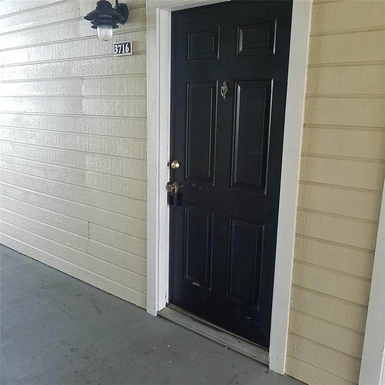 A black front door with a lockbox is set into a light-colored horizontal siding wall — 1017 S HIAWASSEE ROAD UNIT 3716, ORLANDO, FL