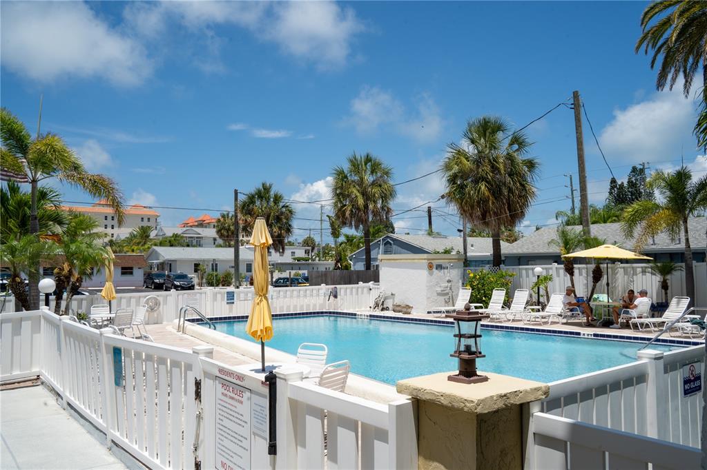 An outdoor swimming pool surrounded by a white fence, lounge chairs, and palm trees — 661 POINSETTIA AVENUE UNIT 108, CLEARWATER BEACH, FL
