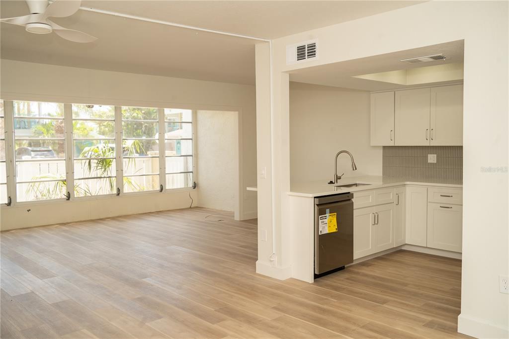 A kitchen with white cabinets and stainless steel appliances opens to a sunroom with windows — 661 POINSETTIA AVENUE UNIT 108, CLEARWATER BEACH, FL