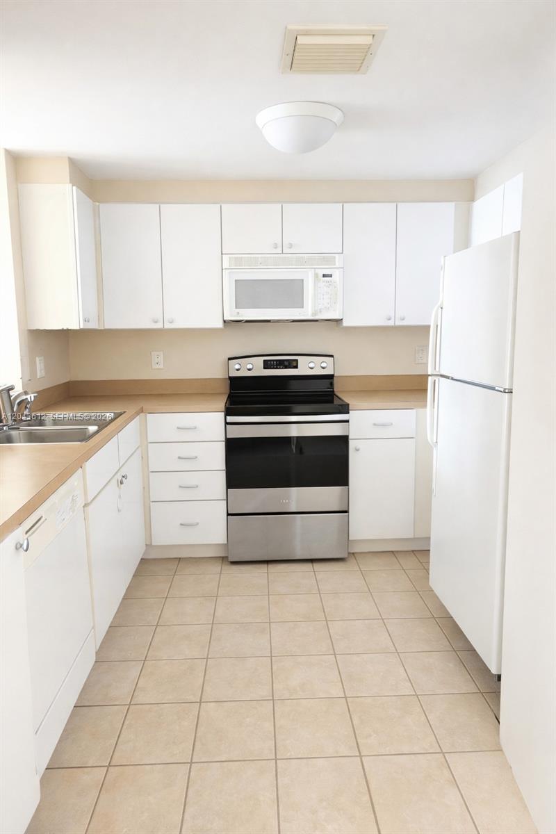 A kitchen features white cabinets, stainless steel appliances, tan tile flooring, and light countertops — 1250 S Miami Ave # 1311, Miami FL 33130, MIAMI, FL