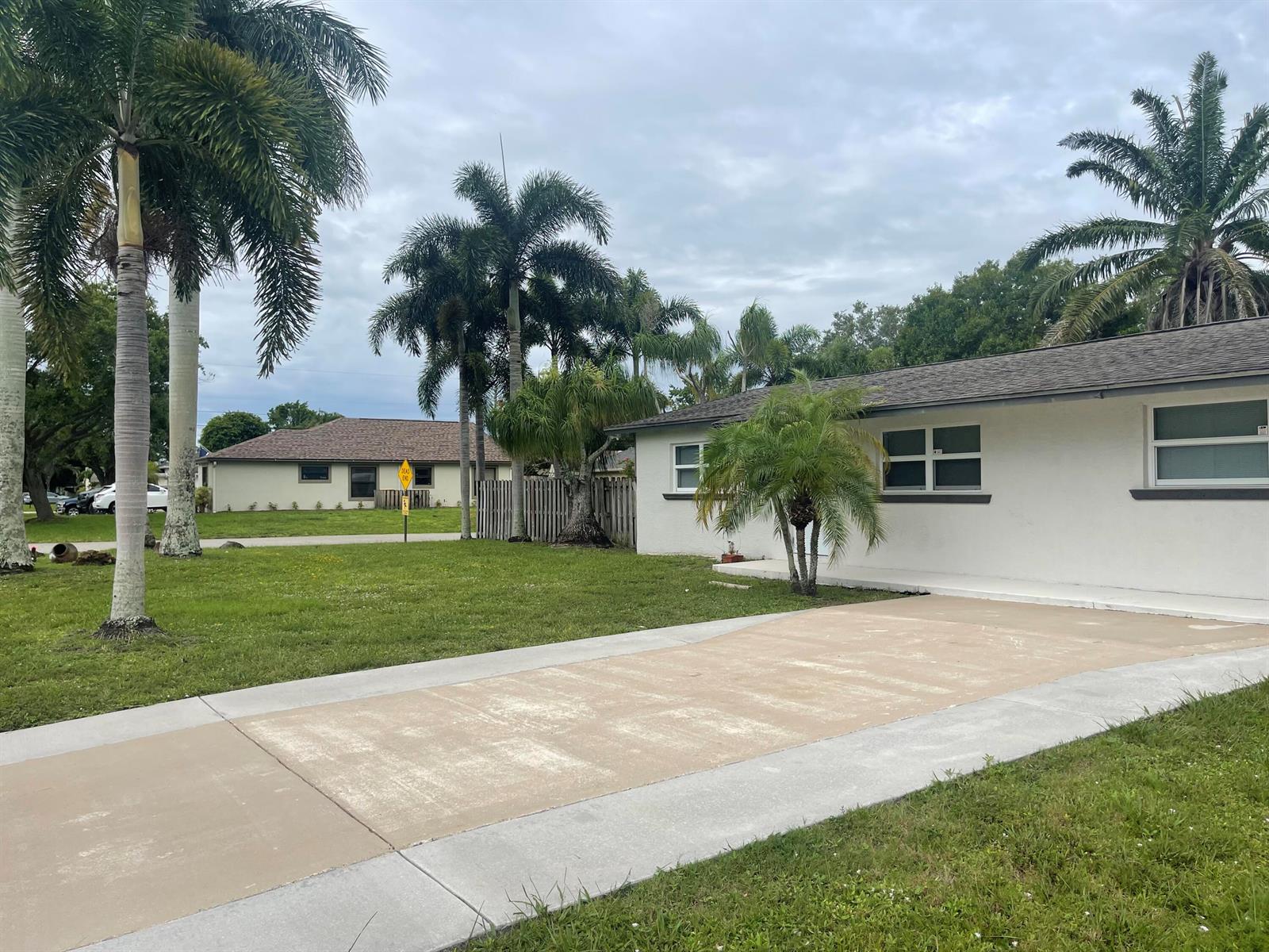 A white single-story house features a concrete driveway and several palm trees in the yard — 4779 Bonanza Road, Lake Worth FL 33467, LAKE WORTH, FL