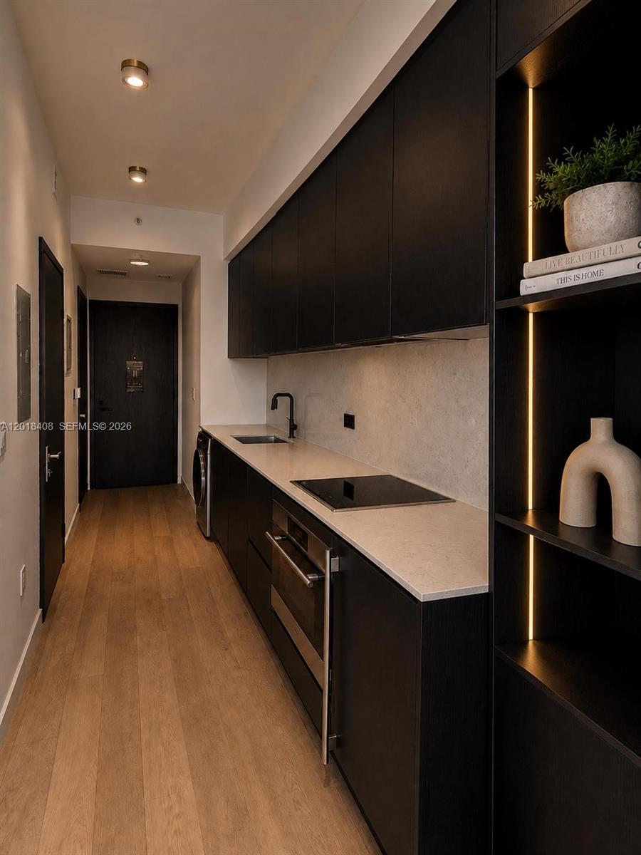 A modern galley kitchen features black cabinetry, light countertops, and wood flooring — 20 NE 11th # 4203A, Miami FL 33132, MIAMI, FL