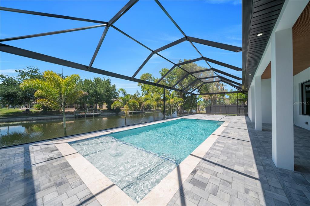 A screened-in pool area with a tanning ledge overlooking a canal and palm trees — 1114 SW 8TH PL, CAPE CORAL, FL