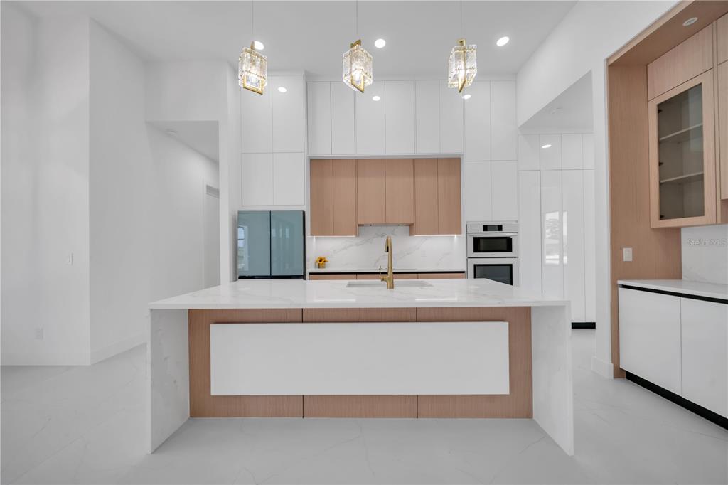 A modern kitchen features white cabinets, light wood accents, a marble island, and three pendant lights — 1114 SW 8TH PL, CAPE CORAL, FL