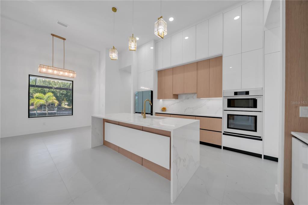 A modern kitchen features white cabinetry, light wood accents, a marble island, and gold fixtures — 1114 SW 8TH PL, CAPE CORAL, FL