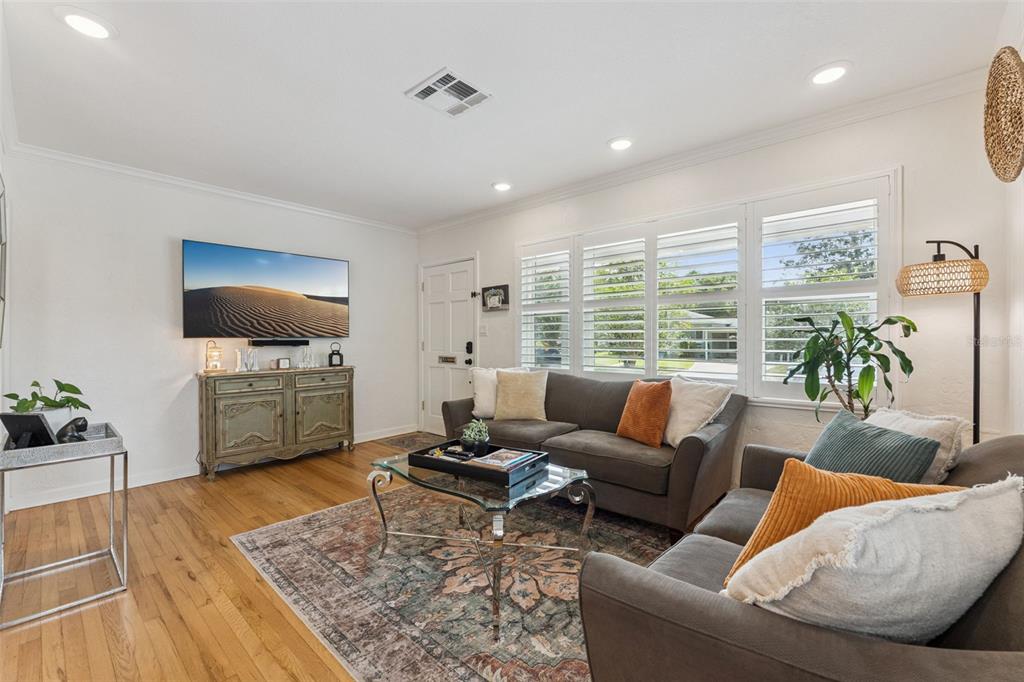 A living room features hardwood floors, two gray sofas, a television, and plantation shutters — 719 WARWICK PLACE, ORLANDO, FL