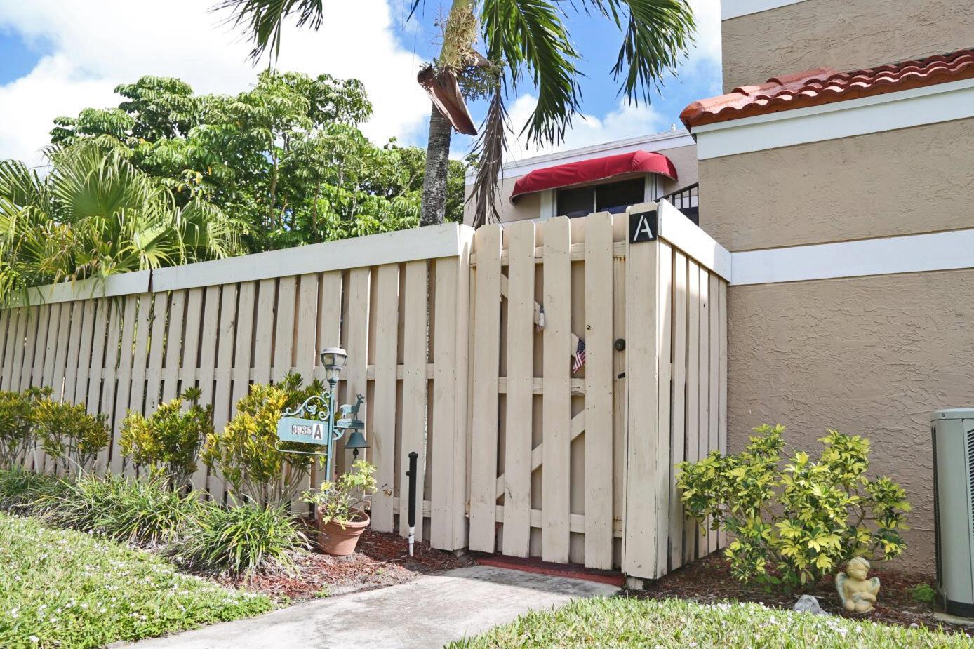 A beige wooden fence with a gate leads to the entrance of a residential unit — 3935 Village Drive # A, Delray Beach FL 33445, DELRAY BEACH, FL