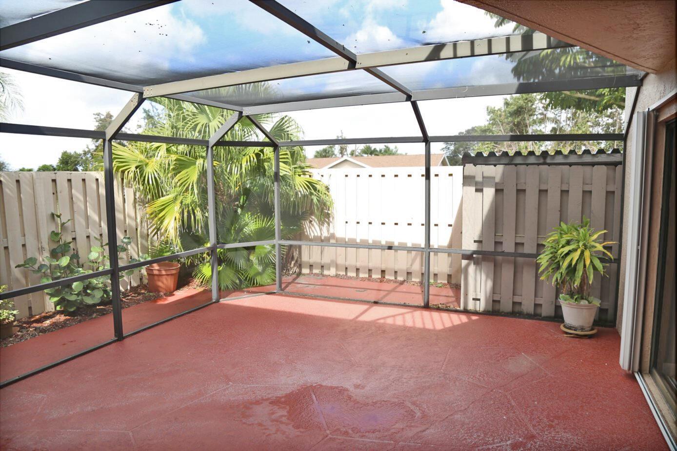 A screened-in patio with a red concrete floor, palm trees, and a wooden privacy fence — 3935 Village Drive # A, Delray Beach FL 33445, DELRAY BEACH, FL