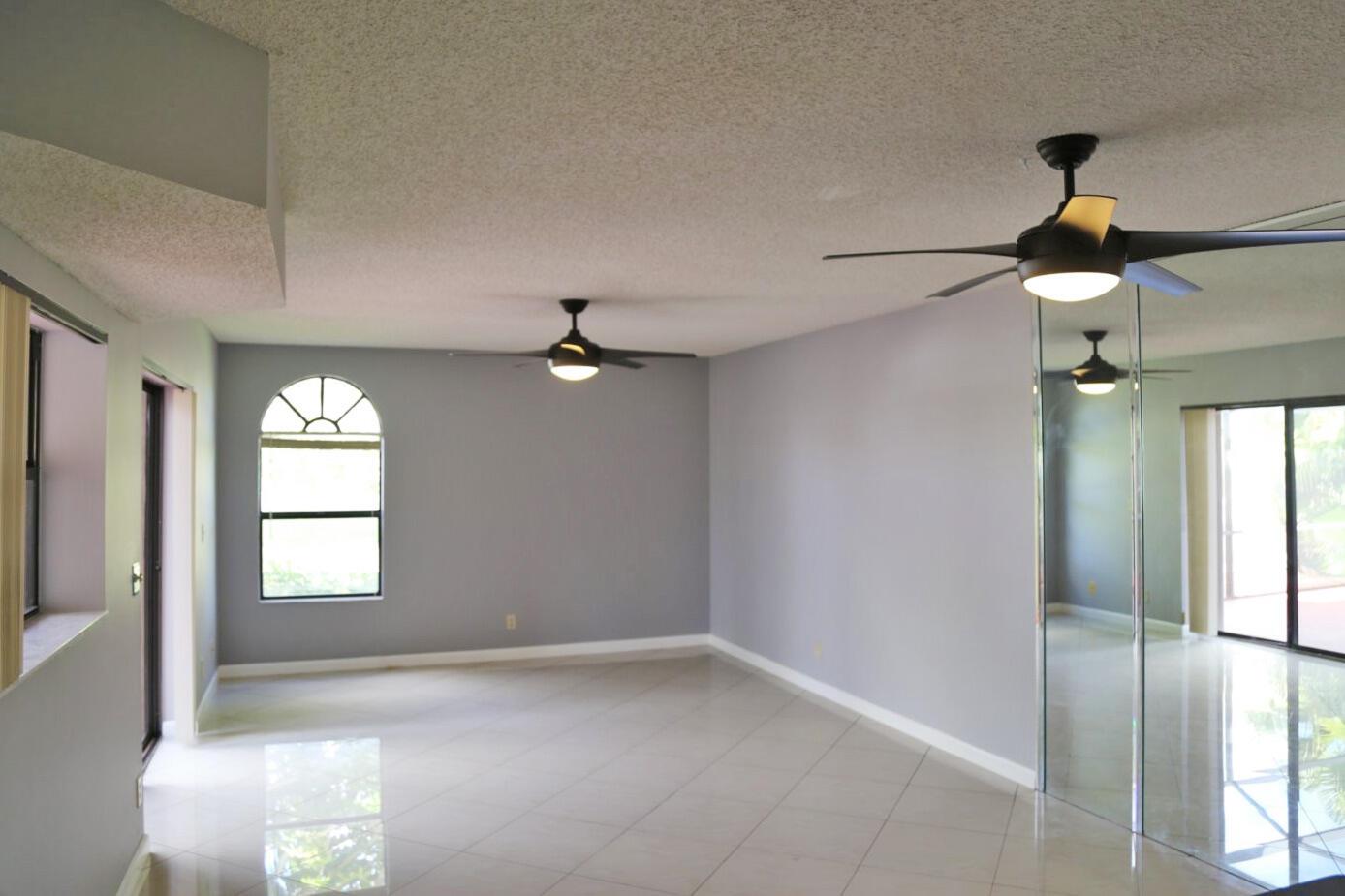 An empty room with gray walls, tile floors, two ceiling fans, and mirrored closet doors — 3935 Village Drive # A, Delray Beach FL 33445, DELRAY BEACH, FL