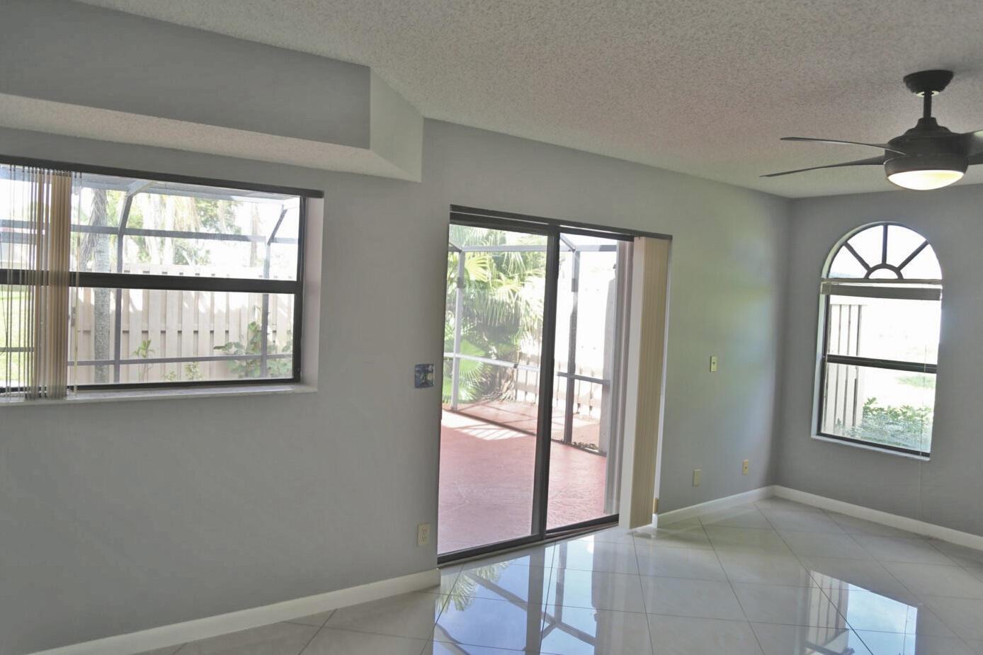 A living room with light gray walls, tile flooring, a ceiling fan, and sliding glass doors — 3935 Village Drive # A, Delray Beach FL 33445, DELRAY BEACH, FL