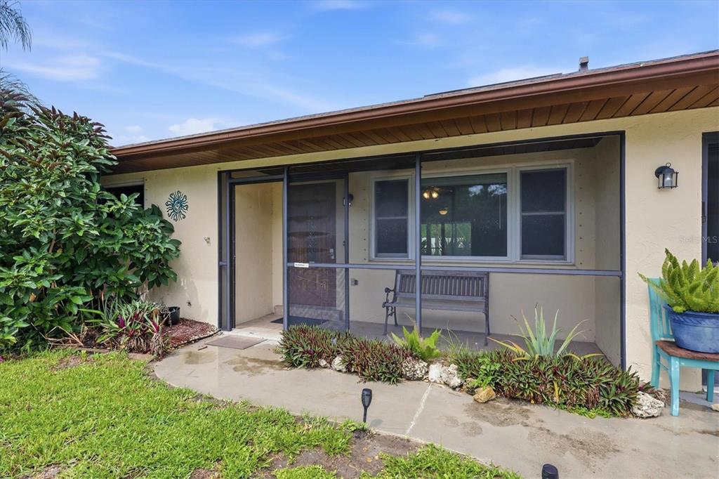 A screened-in front porch features a wooden bench, a front door, and surrounding landscaping — 7067 NATALIE STREET, ENGLEWOOD, FL