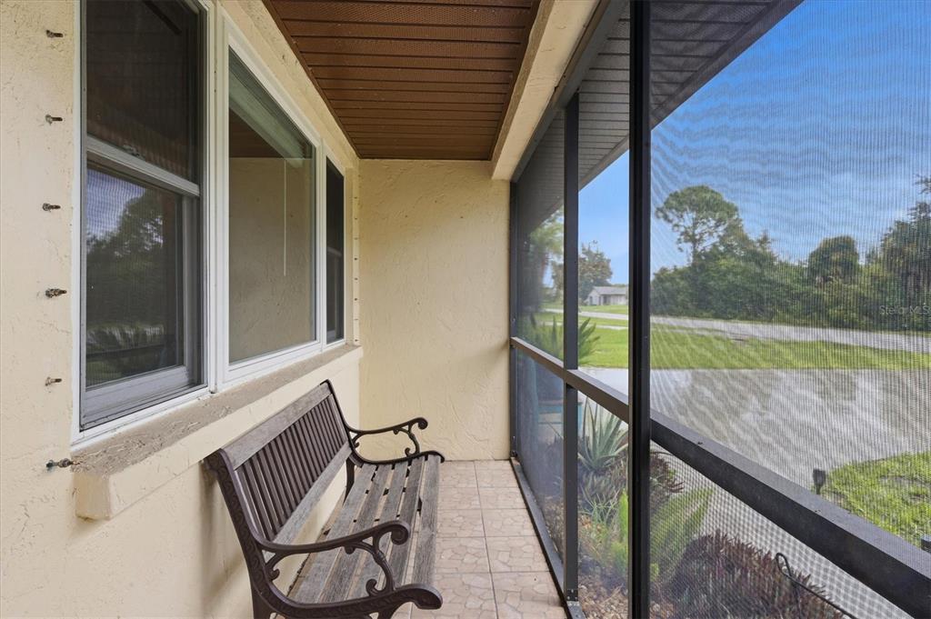 A screened-in porch features a wooden bench, tiled flooring, and views of a grassy yard — 7067 NATALIE STREET, ENGLEWOOD, FL