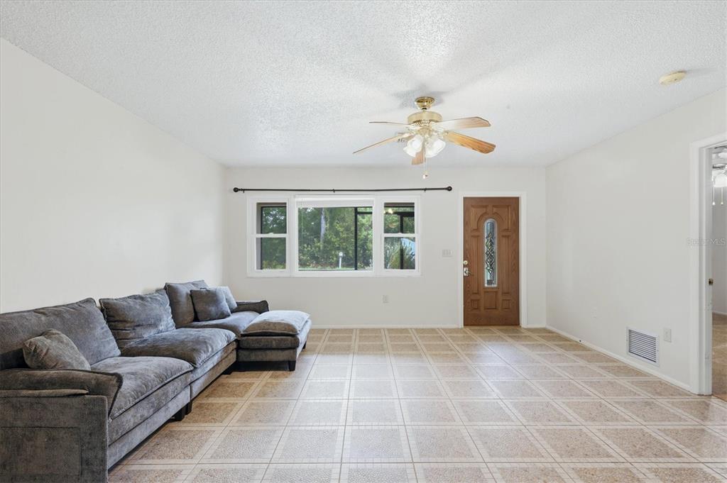A living room features a grey sectional sofa, tiled floors, a ceiling fan, and front door — 7067 NATALIE STREET, ENGLEWOOD, FL