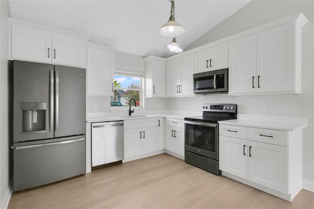 A kitchen with white cabinets, stainless steel appliances, and light wood-look flooring — 9703 RED CLOVER AVENUE, ORLANDO, FL